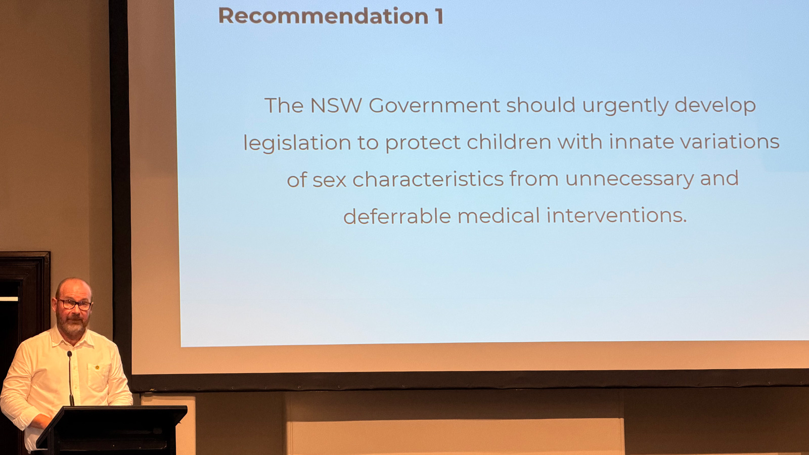 Alastair Lawrie presenting his report, with recommendation 1 on screen: NSW should urgently develop legislation to protect children with innate variations of sex characteristics in medical settings